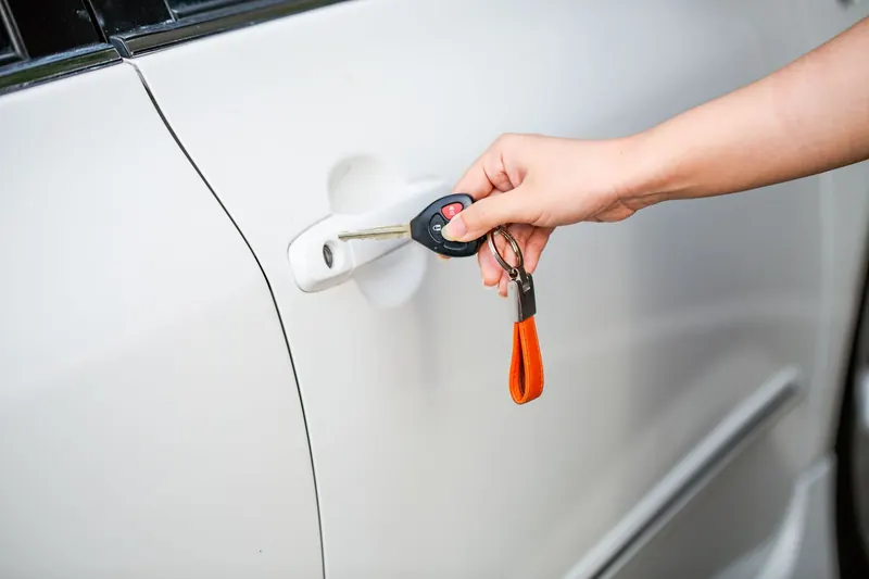 A hand turning a key with a black remote head in the door lock of a white car