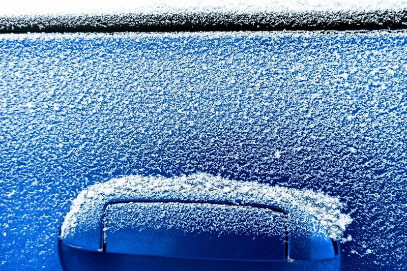 Close-up of a blue car door handle and panel covered in white frost crystals