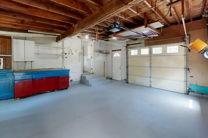 Inside an empty garage, a white sectional door is closed below a ceiling-mounted opener and its rail