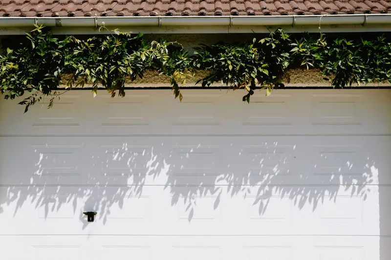 A closed white sectional garage door in sunshine, with leaf shadows across the panels