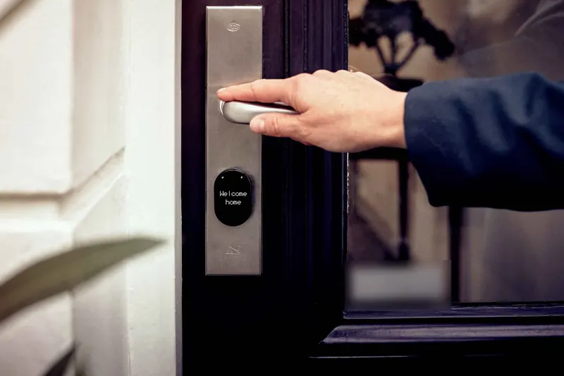 A hand pressing down the lever of an electronic door lock whose small screen reads Welcome home