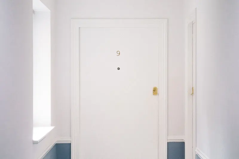 A white apartment door marked with the number 9 at the end of a bright hallway