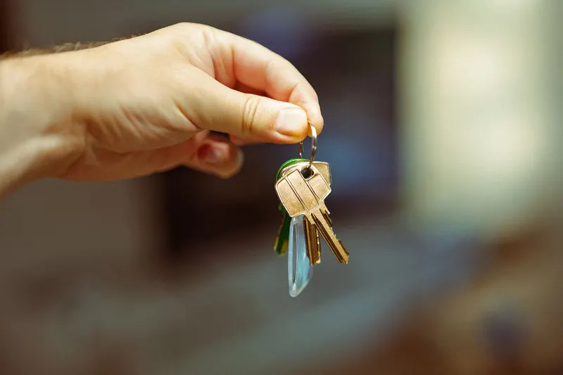 A hand holding up a small ring of brass house keys against a blurred room