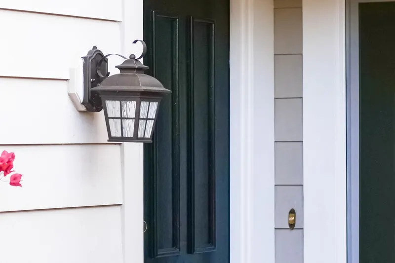 A black front door beside a lantern-style porch light on pale siding