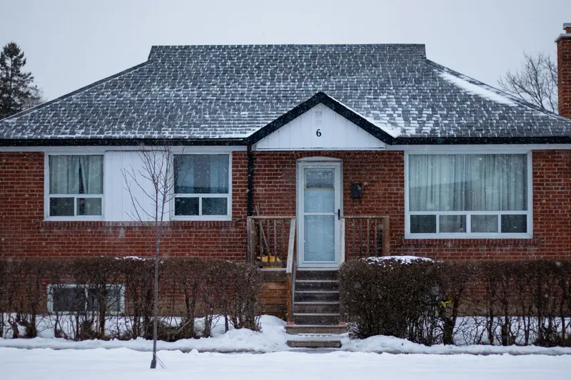 A brick bungalow on a snowy residential street in daylight