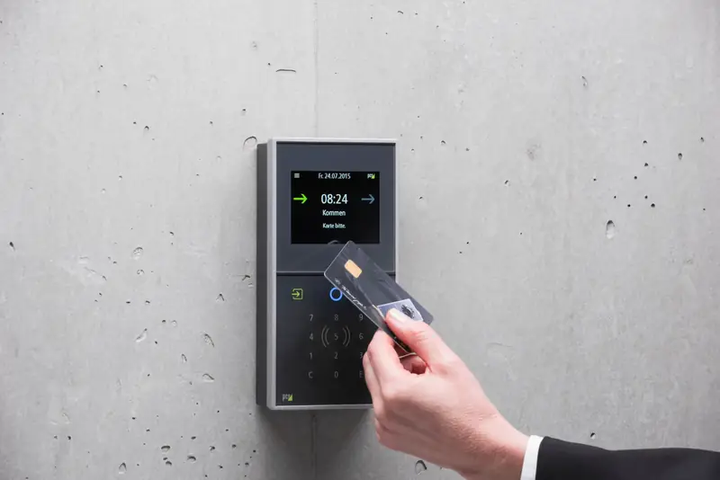 A hand holding an access card up to a wall-mounted reader