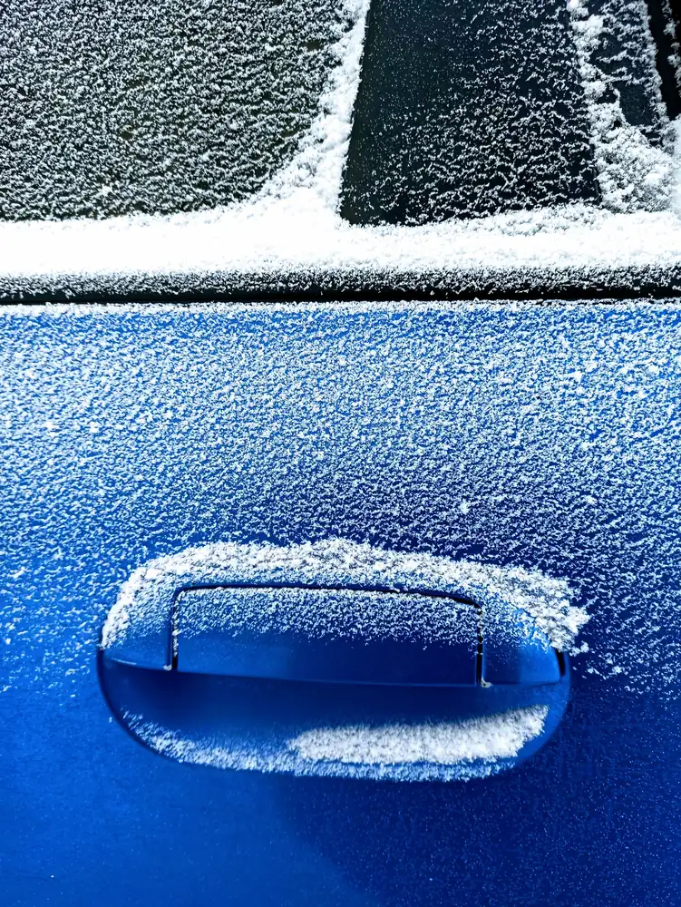 A blue car door handle crusted with frost
