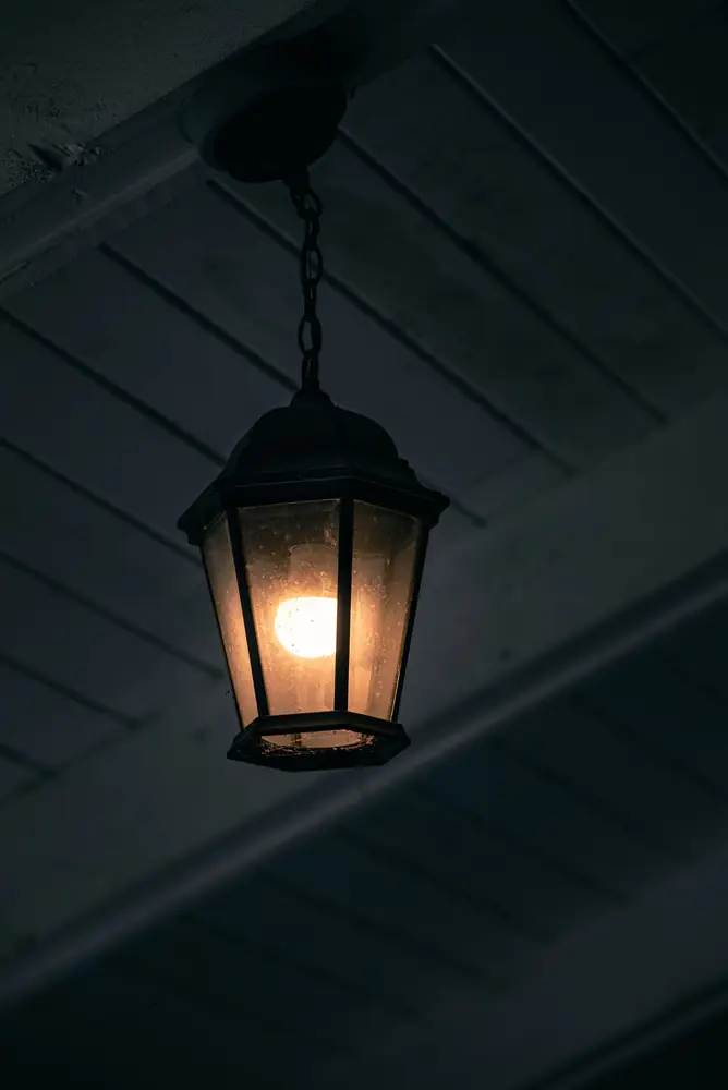A single lantern lit under a dark porch ceiling