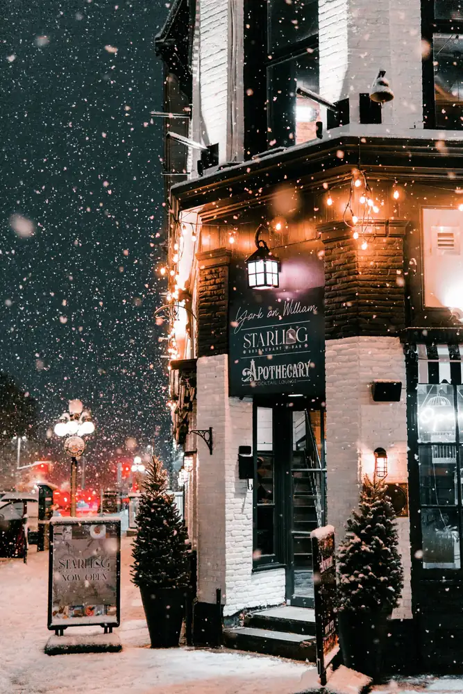 A lit corner shop entrance during a snowstorm at night