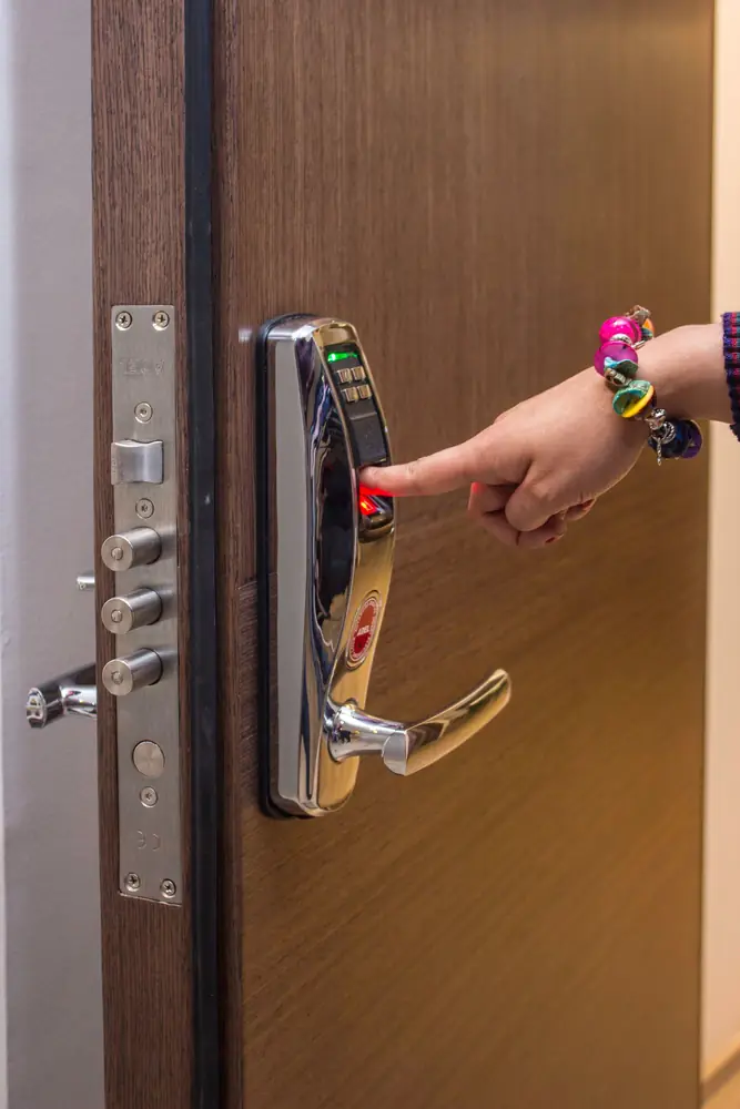 A finger pressing an electronic smart lock on a wooden door